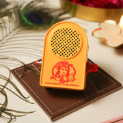A plastic speaker box with a yellow-orange finish, featuring a graphic of Krishna, seated on a brown surface with decorative items in the background.